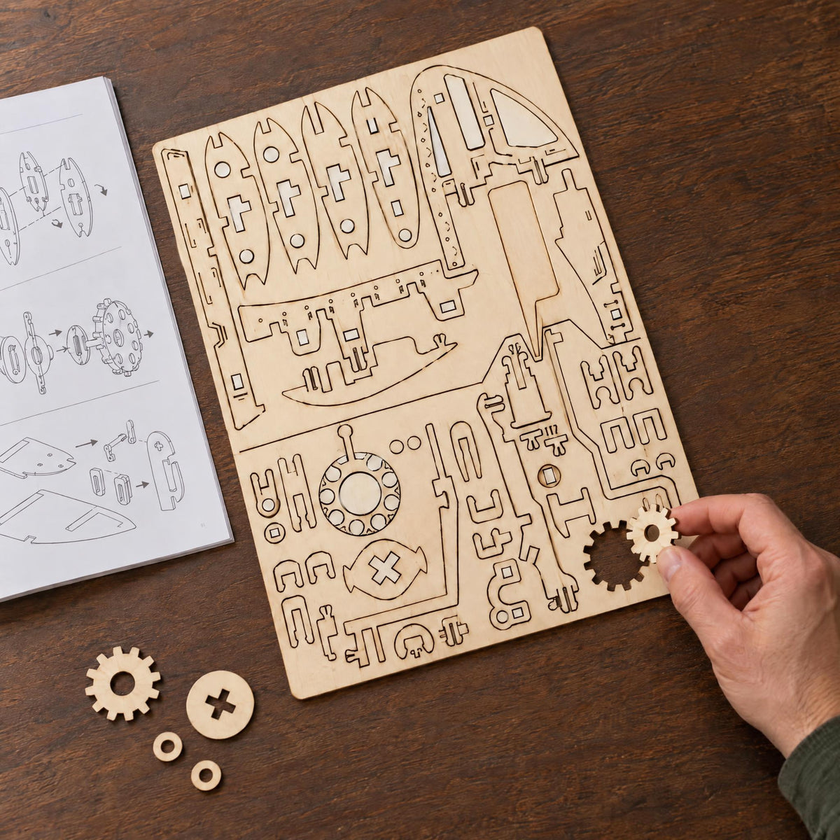 Mechanical airplane, model kit under construction: a hand is removing a gear from the wooden board; next to it are the instructions