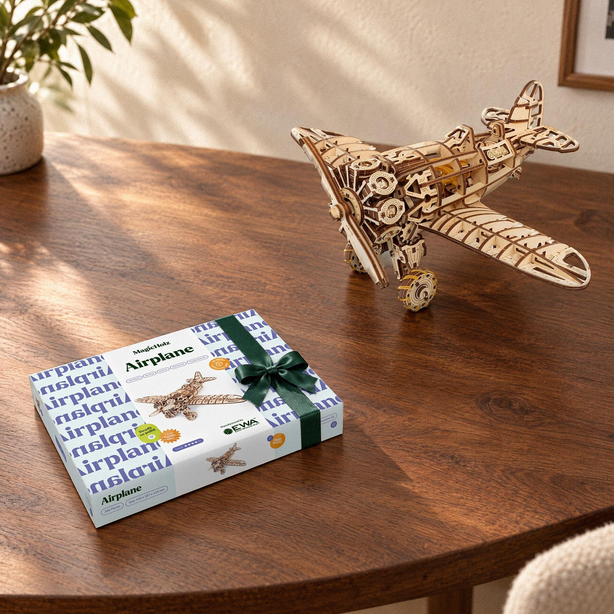 Mechanical airplane: a built wooden model next to the unopened kit box with a green bow on a wooden table