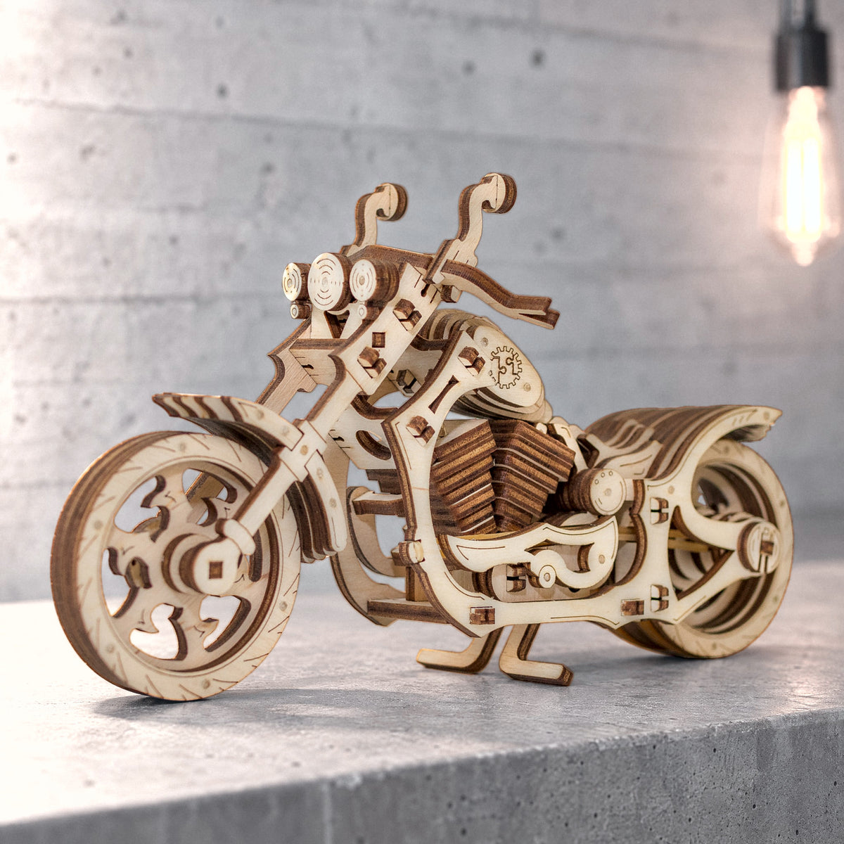 Cruiserfiets, houten model van een motorfiets op een betonnen stoeprand voor een lichte, zichtbetonnen muur in een loft, het warme licht van een gloeilamp