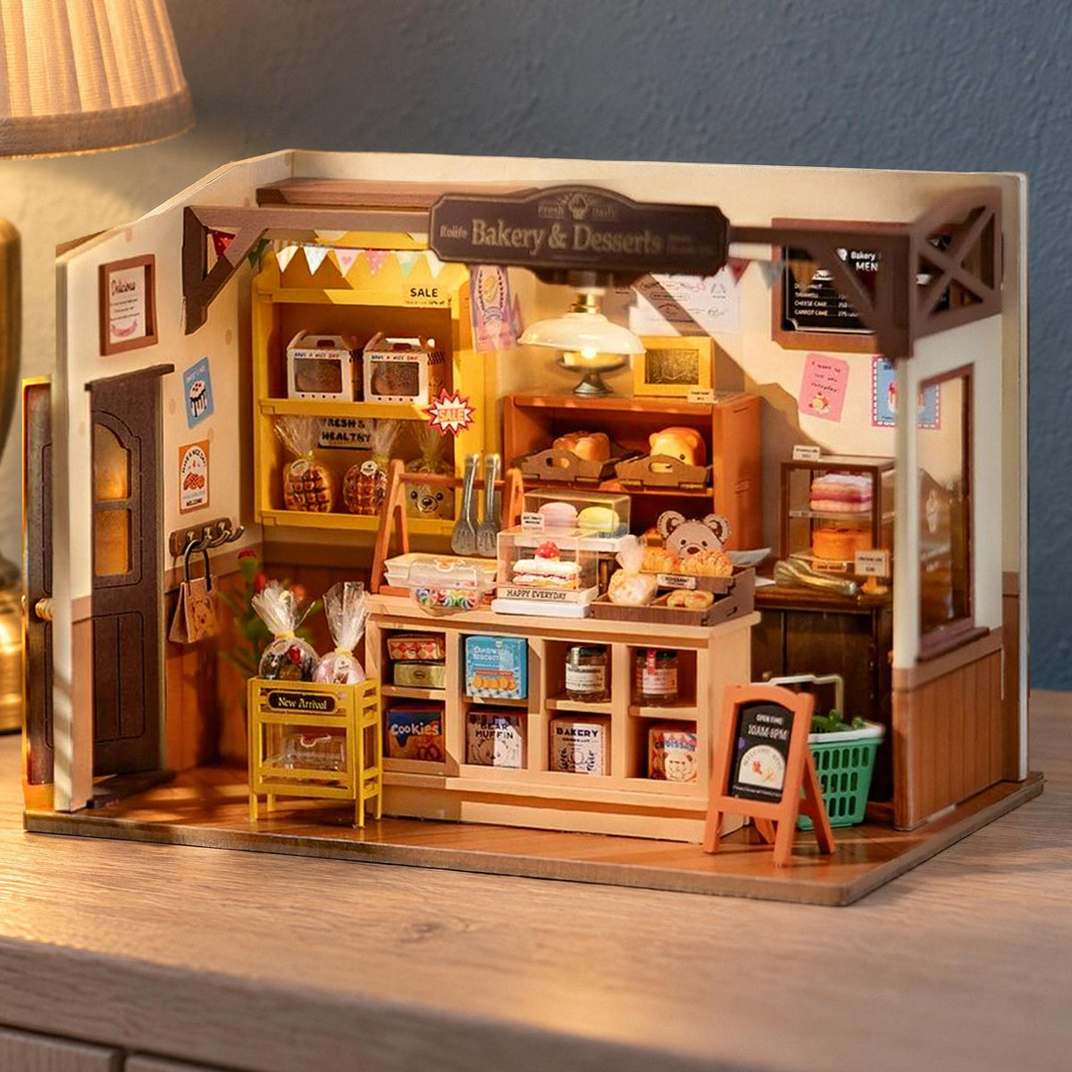 Becka’s Baking House (bakery) miniature house, lit up in the early evening on a light-colored sideboard against a blue wall