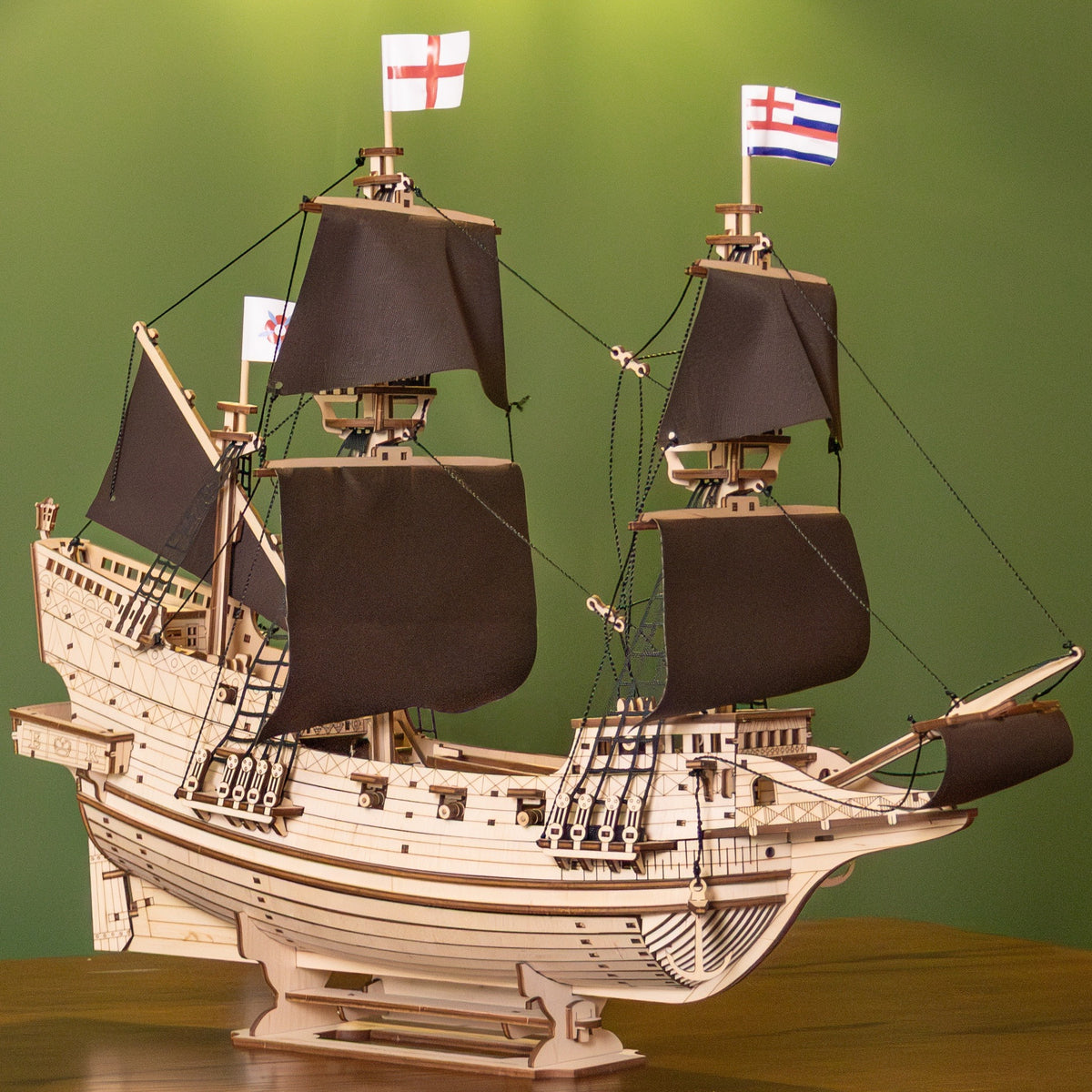 "Lord of the Seas" Wooden Sailing Ship Model Kit, a finished three-masted ship with black sails on a wooden table in front of a green wall