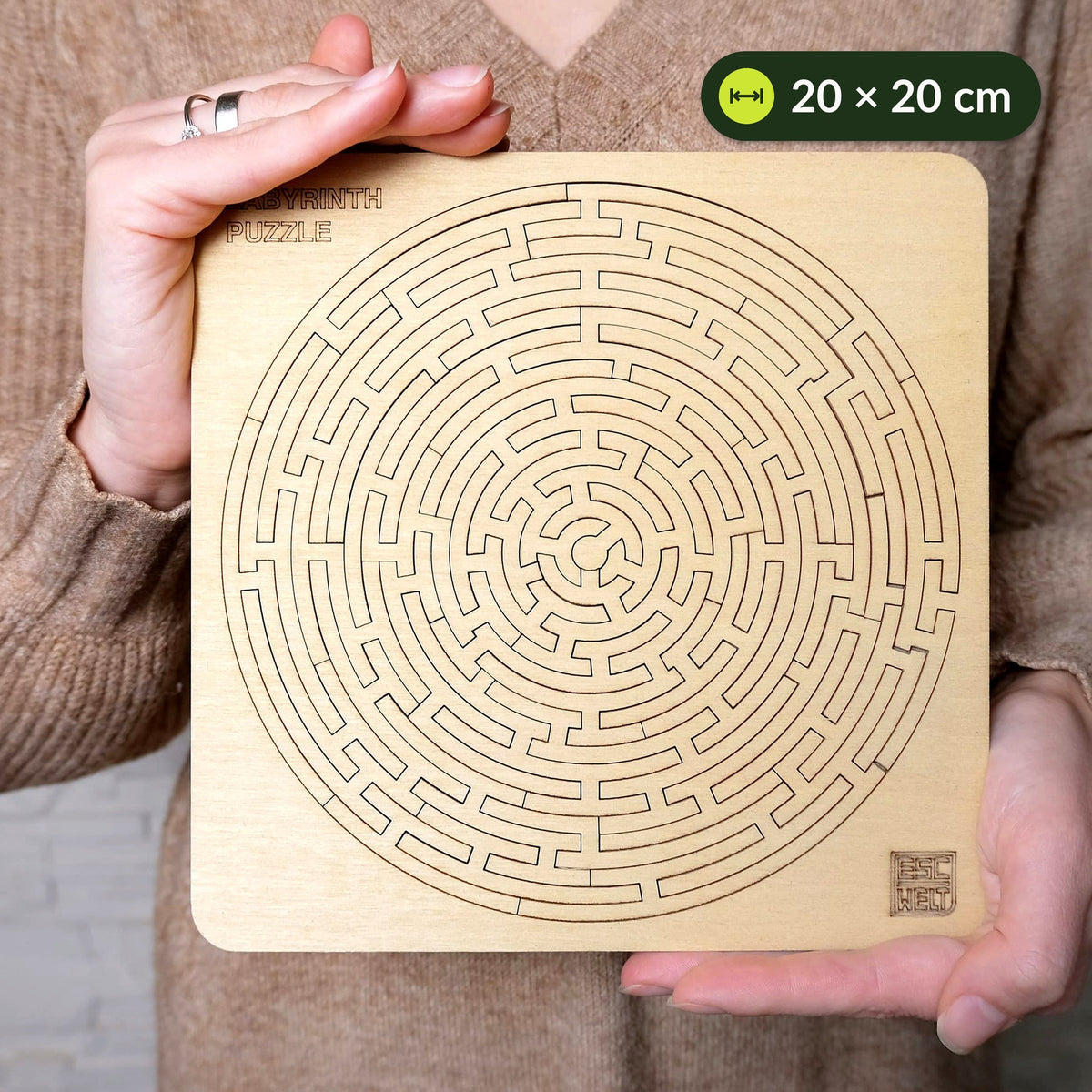 A maze puzzle held in both hands in front of a knitted sweater, measuring about 20 x 20 cm