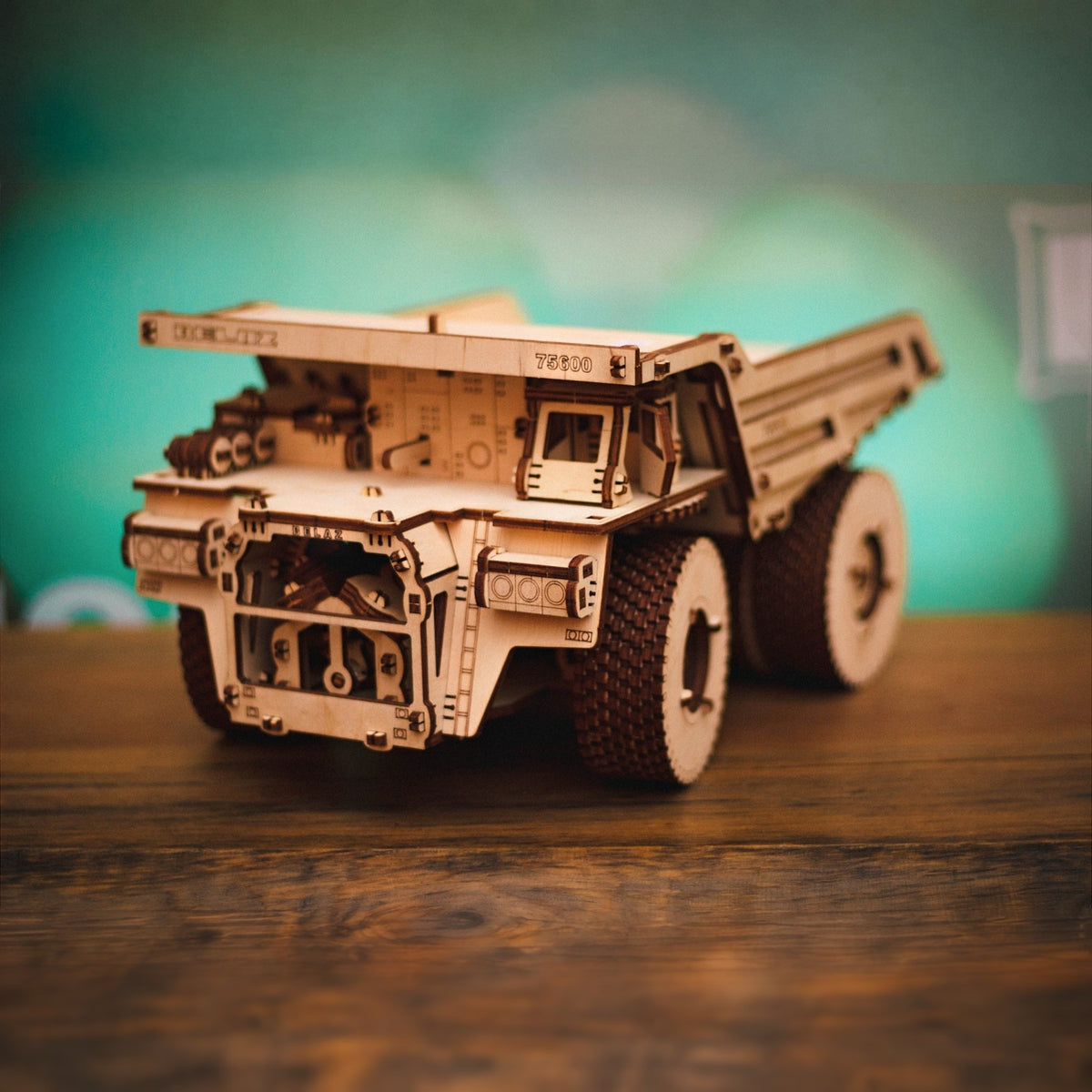 BELAZ 75600 Muldenkipper aus Holz auf einem dunklen Holztisch vor türkiser Wand, mechanischer Bausatz