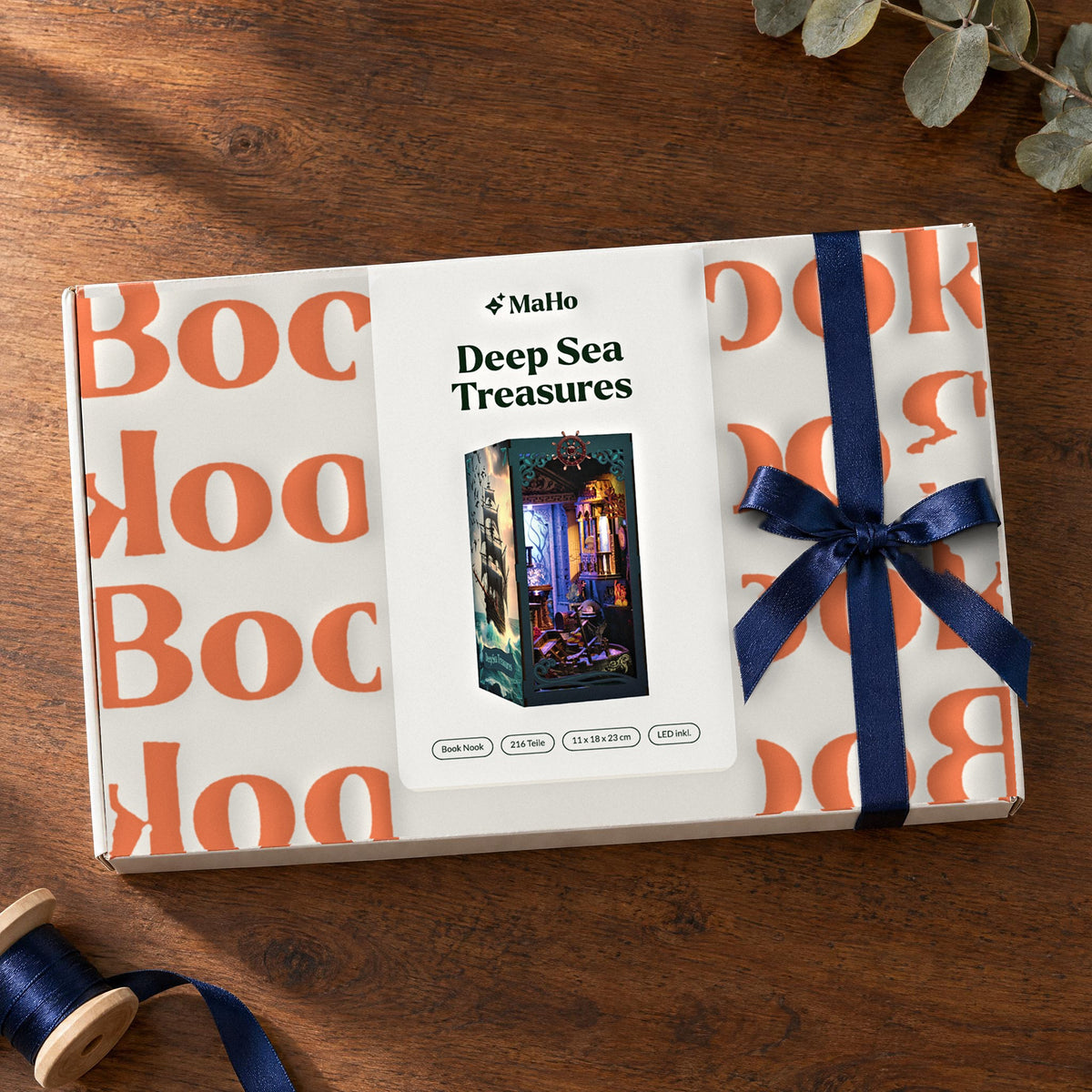 Deep Sea Treasures Book Nook, en cadeau : boîte MaHo fermée, ornée d'un nœud en satin bleu, posée sur une table en noyer