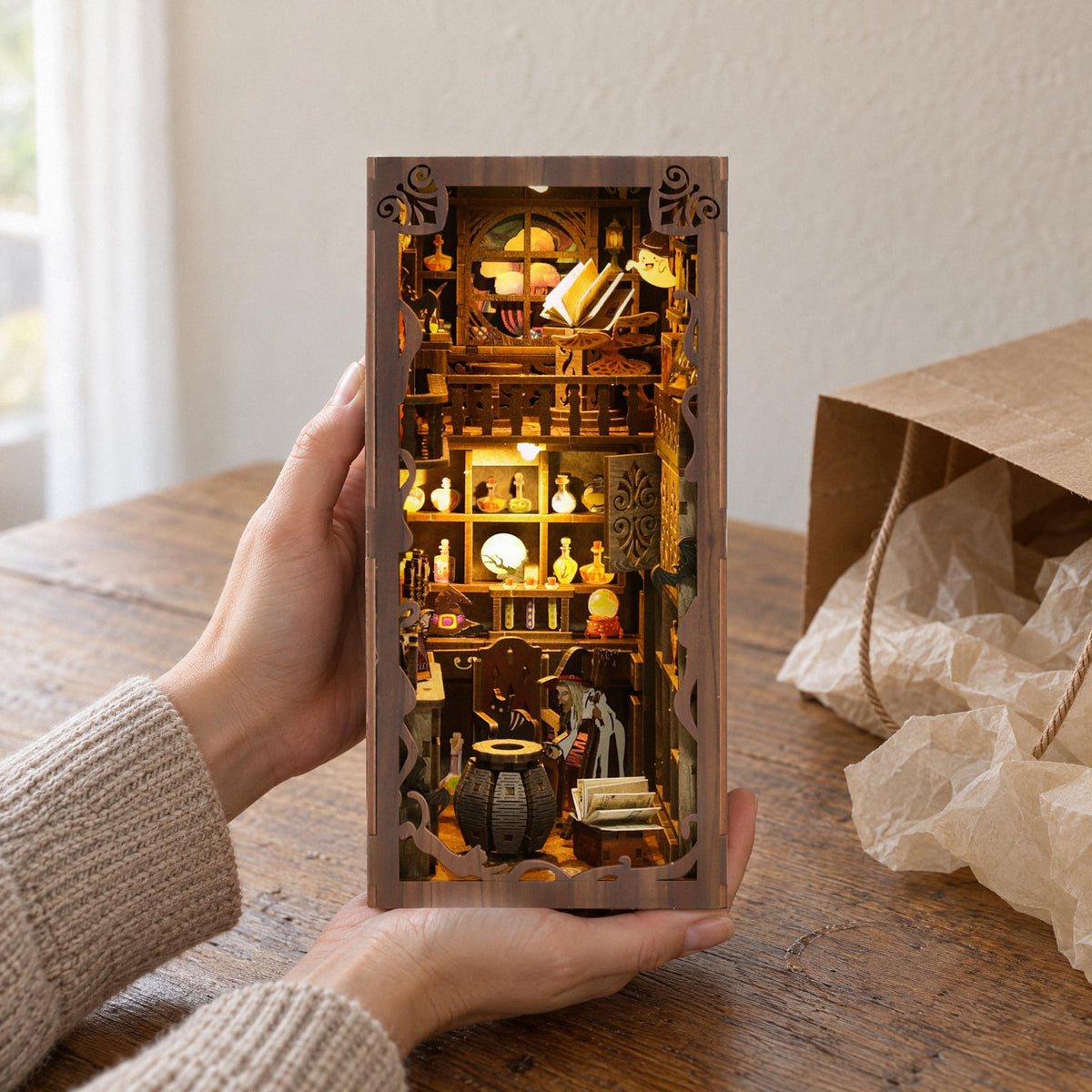 MagicNight Book Nook, cadeaumoment: handen halen het verlichte diorama uit een zak van pakpapier