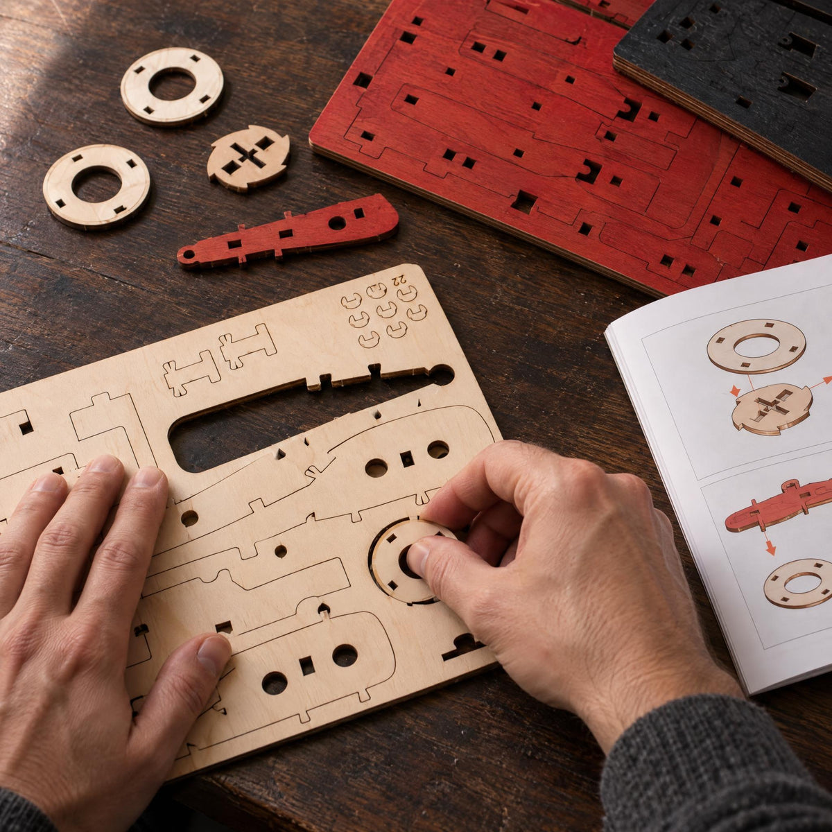 Kit de voiture de course, les mains détachent une pièce ronde de la plaque de bois découpée au laser, à côté se trouvent les instructions