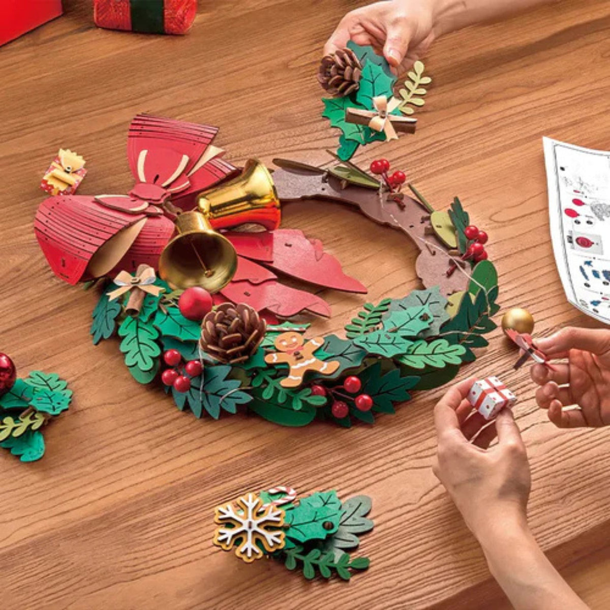 3D-puzzel met kerstkrans: tijdens het in elkaar zetten leg je met je handen de blaadjes en versieringen op de kransring; ernaast ligt de handleiding