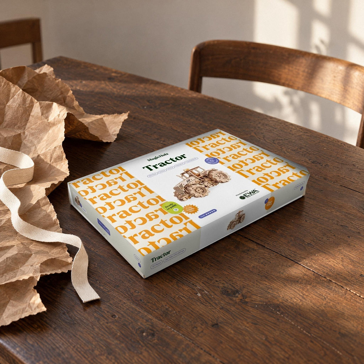 Un tracteur mécanique, offert en cadeau : un carton fermé posé sur la table à manger, avec à côté du papier d'emballage et un ruban en coton