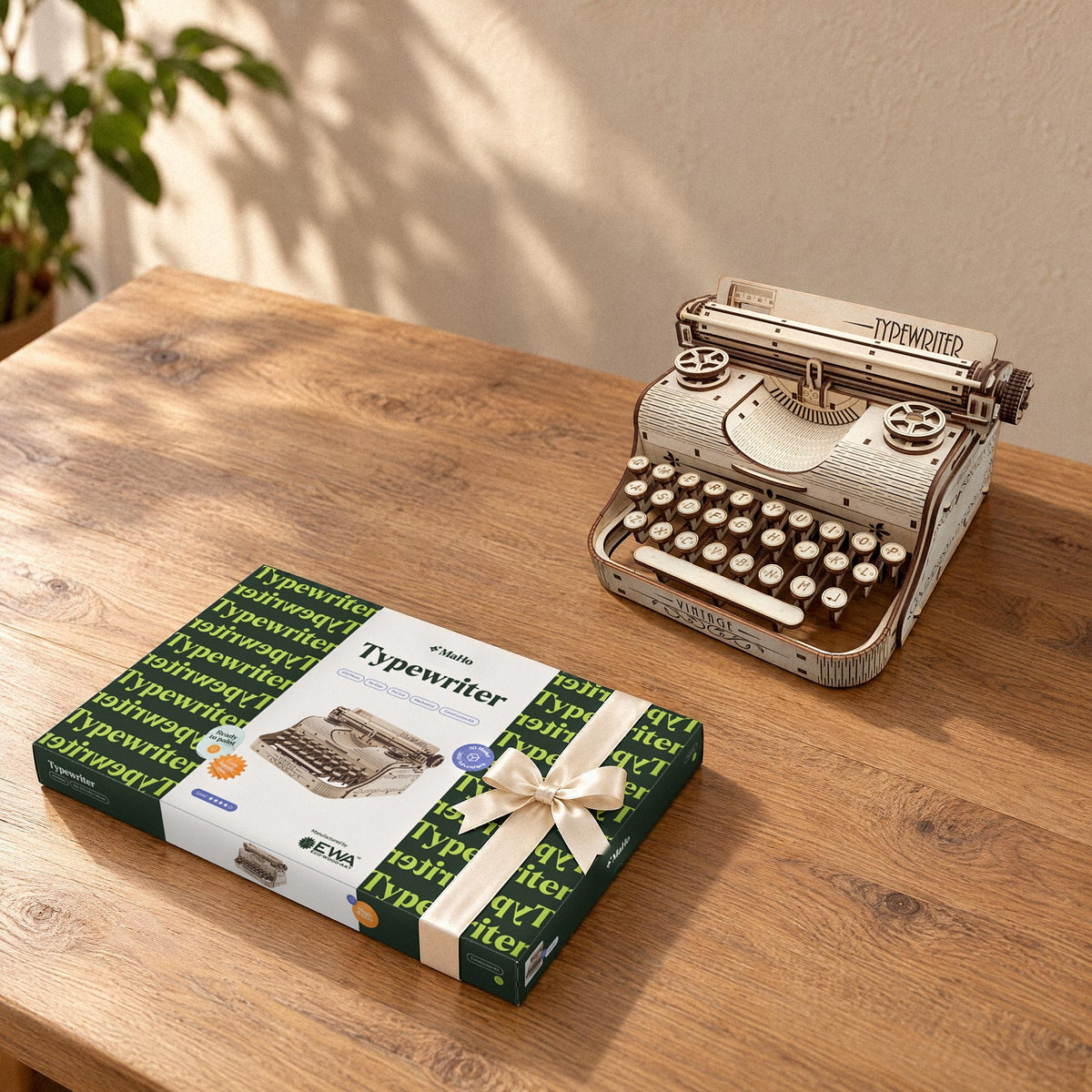 Schreibmaschine – Vintage Typewriter, gebautes Holzmodell neben dem geschlossenen Bausatz-Karton mit Schleife auf einem Tisch