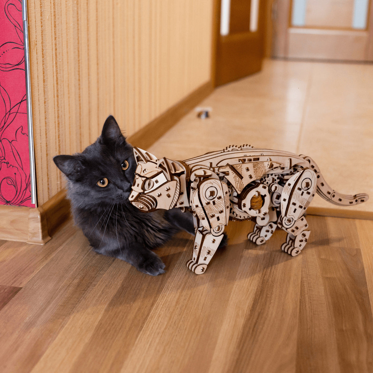 Mechanische katten – naturel of zwart, een naturelgekleurde houten kat op parket, ernaast snuffelt een echte zwarte kat