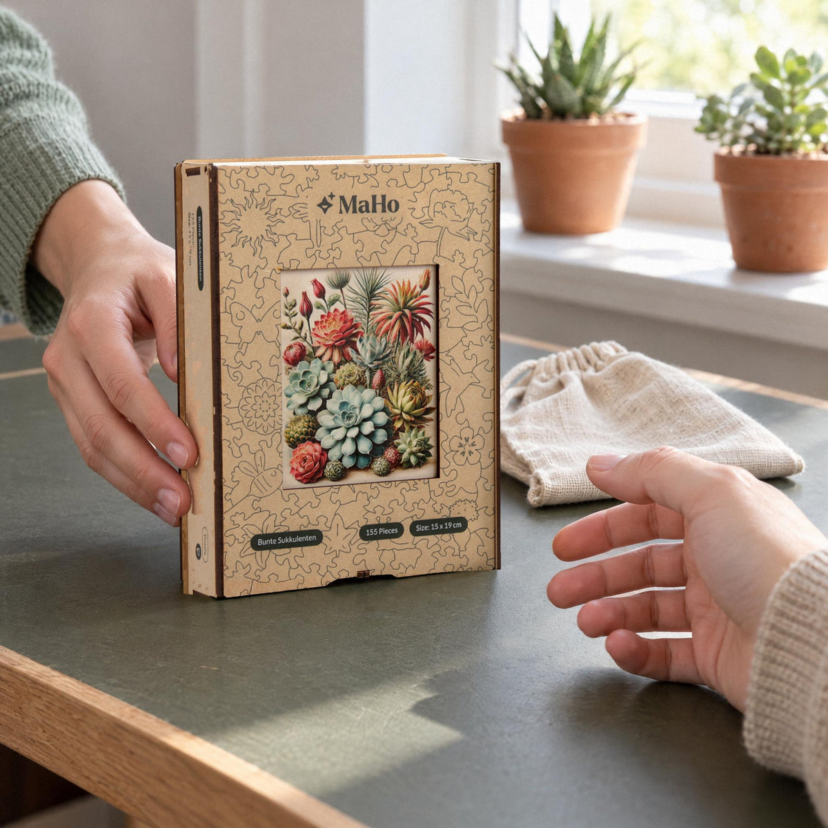 Bunte Sukkulenten Holzpuzzle, Premium-Holzbox mit Motiv wird als Geschenk über den Tisch gereicht, daneben der Stoffbeutel