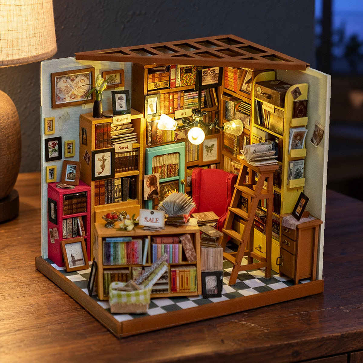 La maison miniature « Sam's Study », un bureau éclairé avec des étagères posées sur un buffet en noyer, le soir