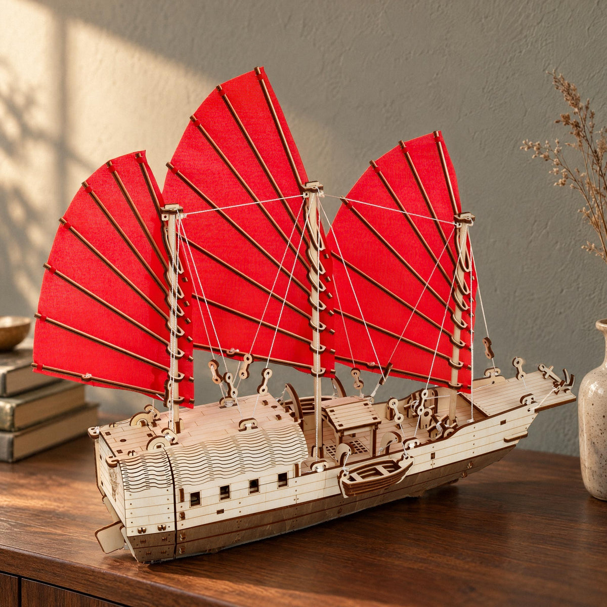 Un bateau Djong en bois aux voiles rouges posé sur un buffet en noyer dans le salon, sous une lumière chaleureuse
