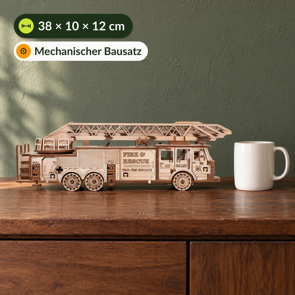 Mechanischer LKW Feuerwehrauto Holzbausatz, 38 cm langes Modell neben einer Tasse auf Nussbaum-Sideboard vor grüner Wand