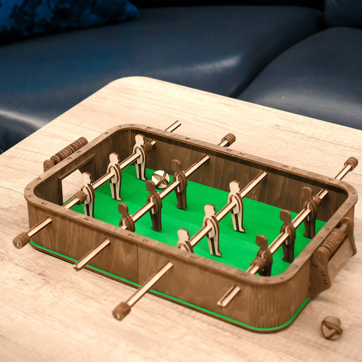A wooden foosball table on a light-colored coffee table in front of a dark blue leather sofa in the living room