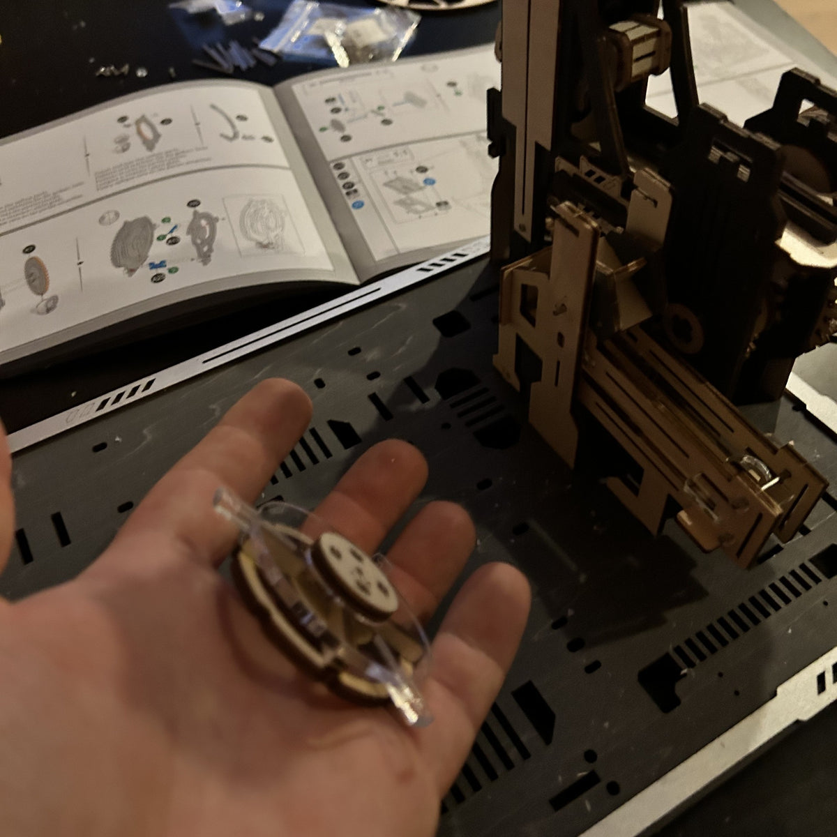 Marble Spaceport wooden marble run, under construction: A hand is holding a spiral piece; behind it are the instructions and a partially assembled model