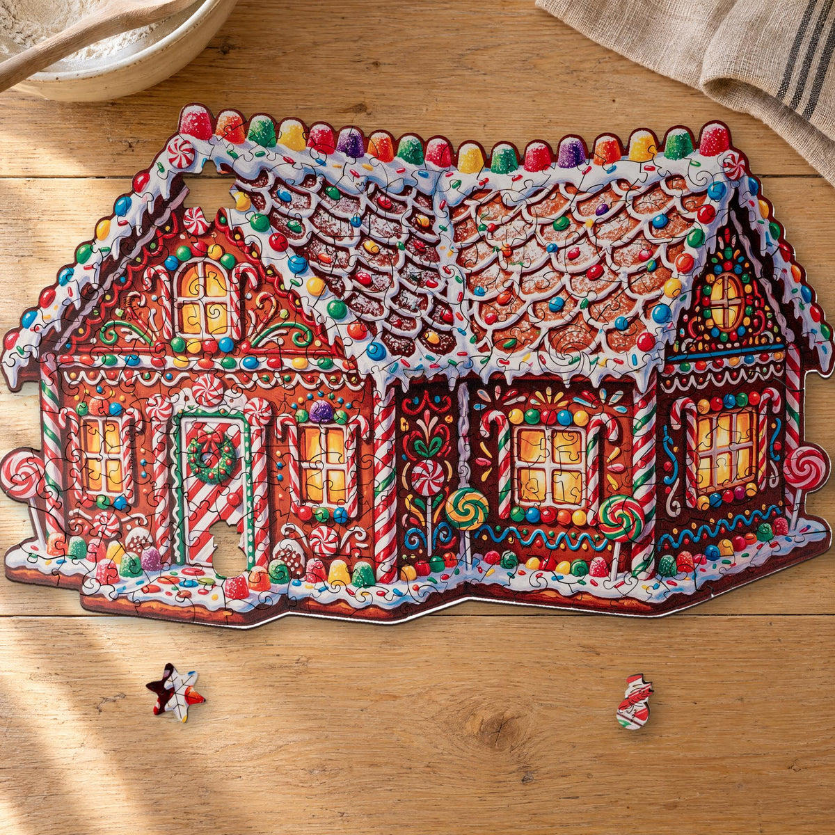 Märchenhaftes Lebkuchenhaus Holzpuzzle, fast fertig auf einem hellen Eichentisch, davor Stern und Schneemann als Figurenteile