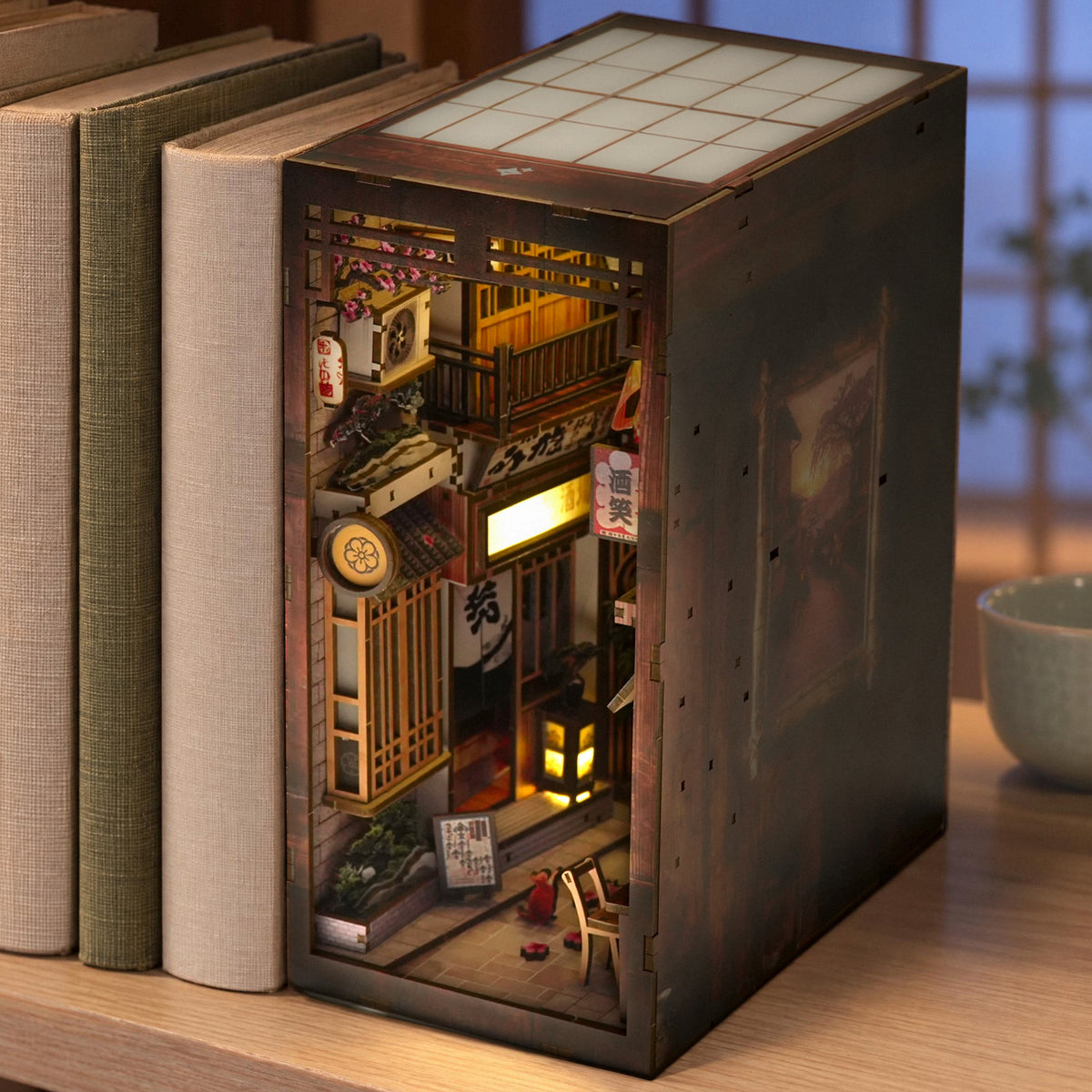 Traditional Japanese Alley Book Nook: a glowing Japanese alley serving as a bookend on a light-colored shelf next to linen-bound books in the evening