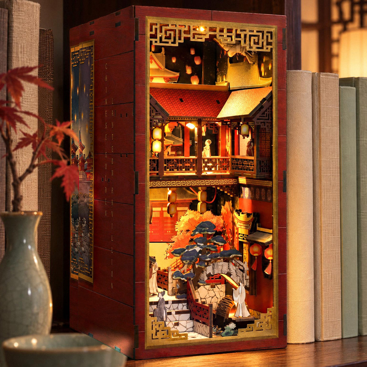 Chinese Golden Lantern Pavilion Book Nook, illuminated in the evening on the shelf next to bright-colored books and a vase
