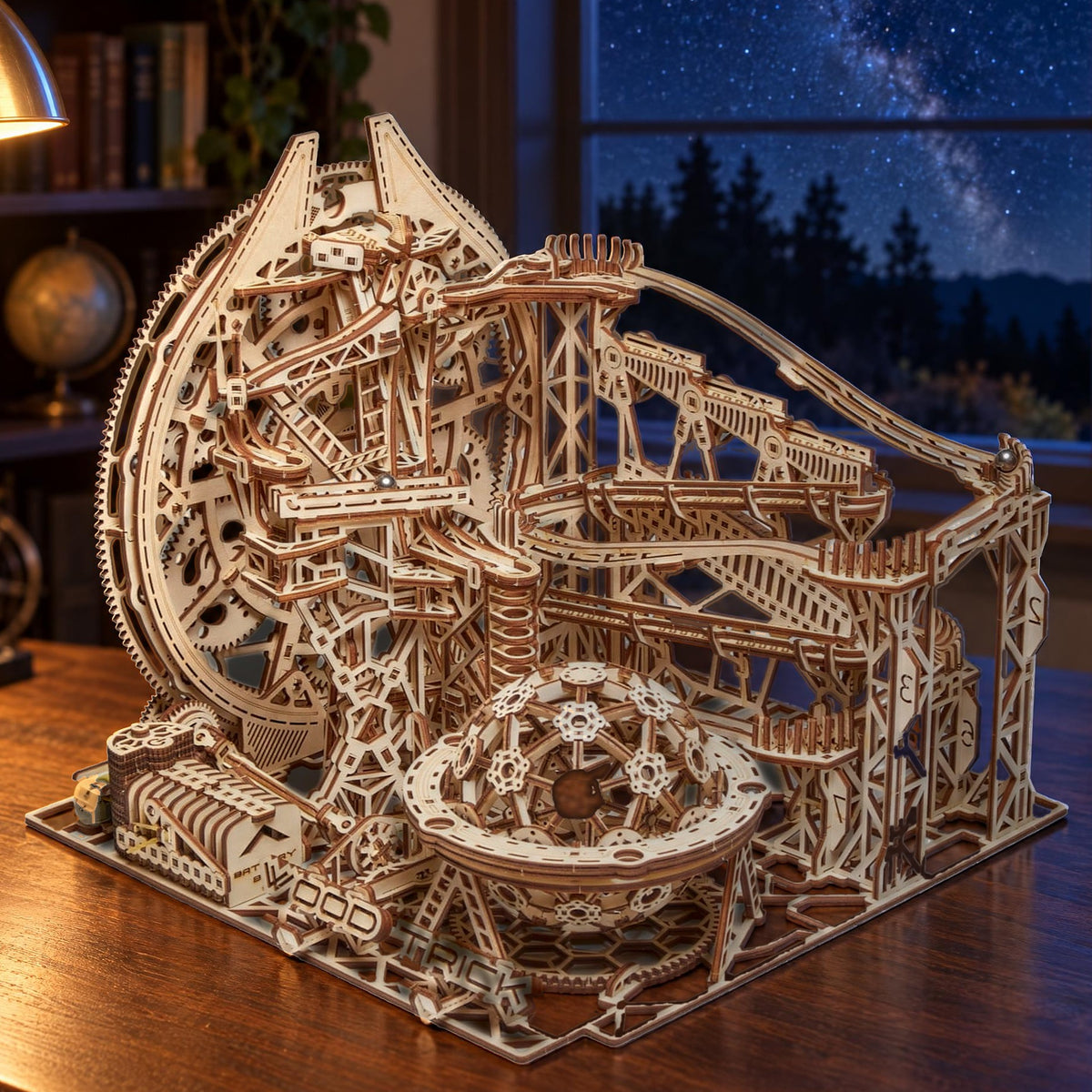 Un circuit à billes « Galaxy » en bois, posé sur un bureau près de la fenêtre, avec dehors la Voie lactée et le ciel nocturne, à la lueur chaleureuse d'une lampe