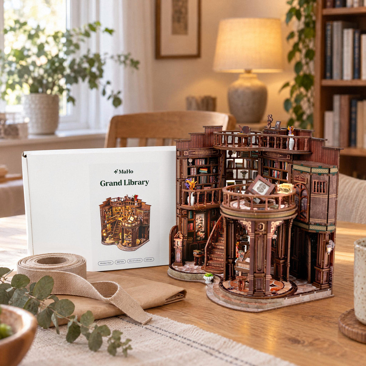 Grand Library Miniaturhaus fertig gebaut neben dem MaHo-Karton auf dem Esstisch, mit Geschenkband und Packpapier