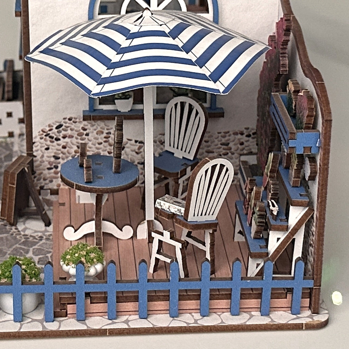 Santorini Café Miniaturhaus, Einblick in die Terrasse: Sonnenschirm, Tisch, Stühle und Blumen