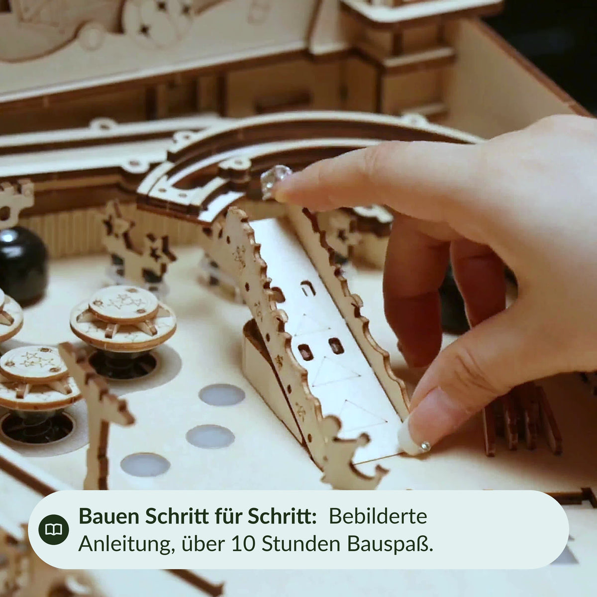 Une main insère une pièce en bois dans le flipper 3D, notice illustrée, plus de 10 heures de plaisir à le monter