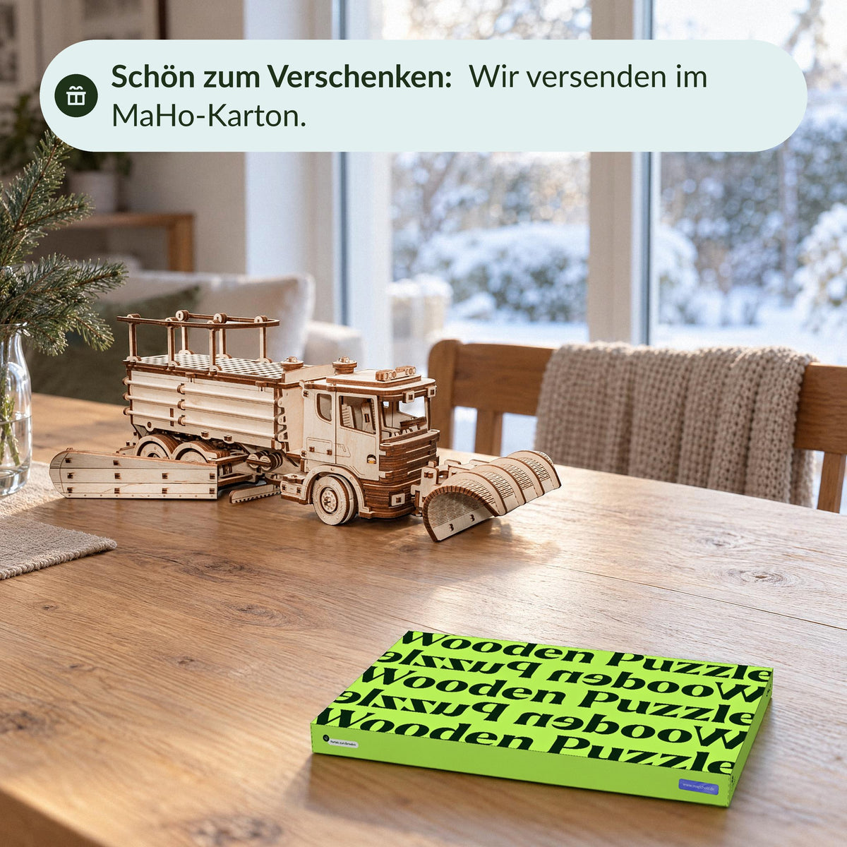 Geschenkmoment am Esstisch im Winter: Schneeräumer aus Holz mit allen Pflügen, davor der geschlossene grüne MaHo-Karton