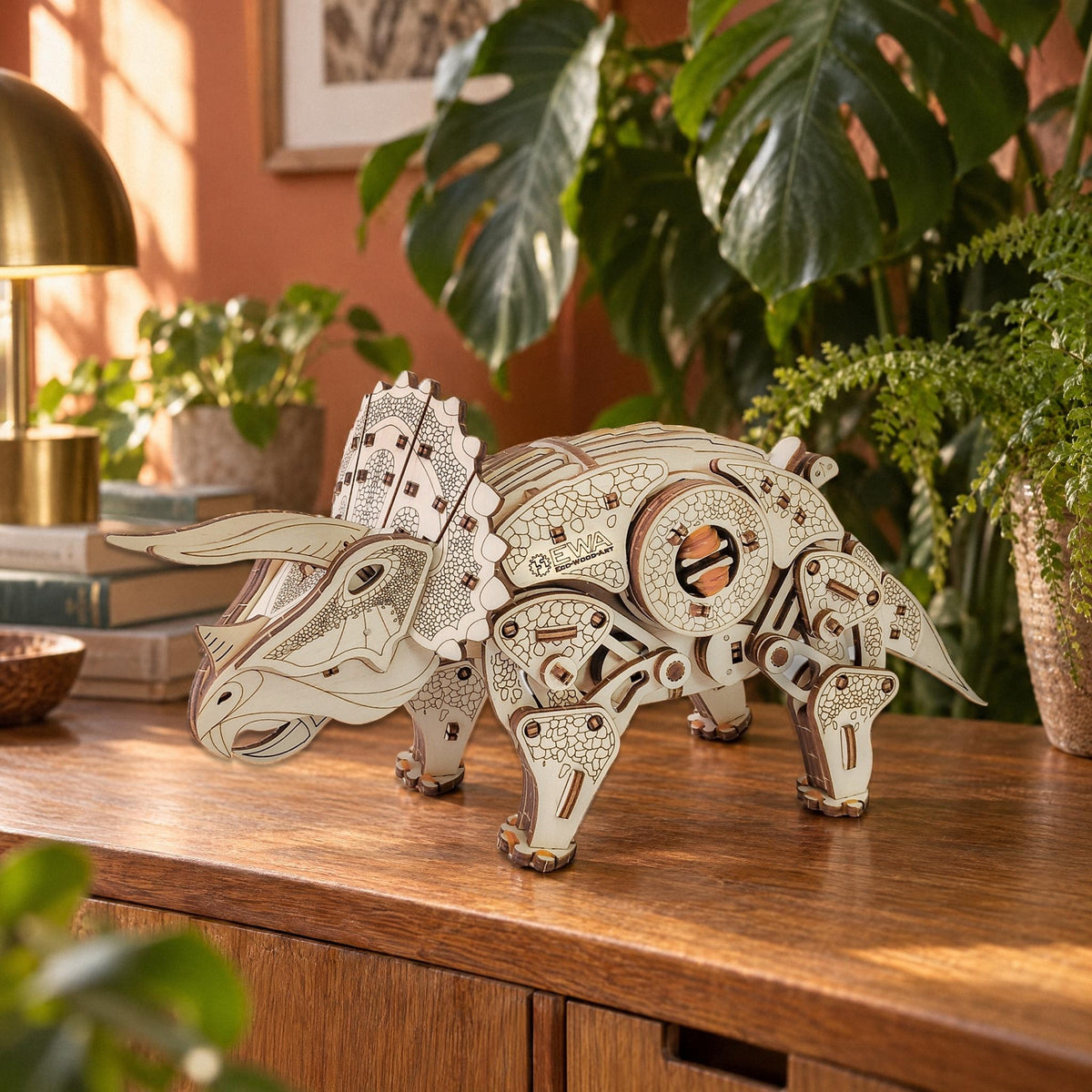 Triceratops aus Holz auf einem Eichen-Sideboard zwischen Monstera und Farnen, Nachmittagslicht, mechanischer Bausatz