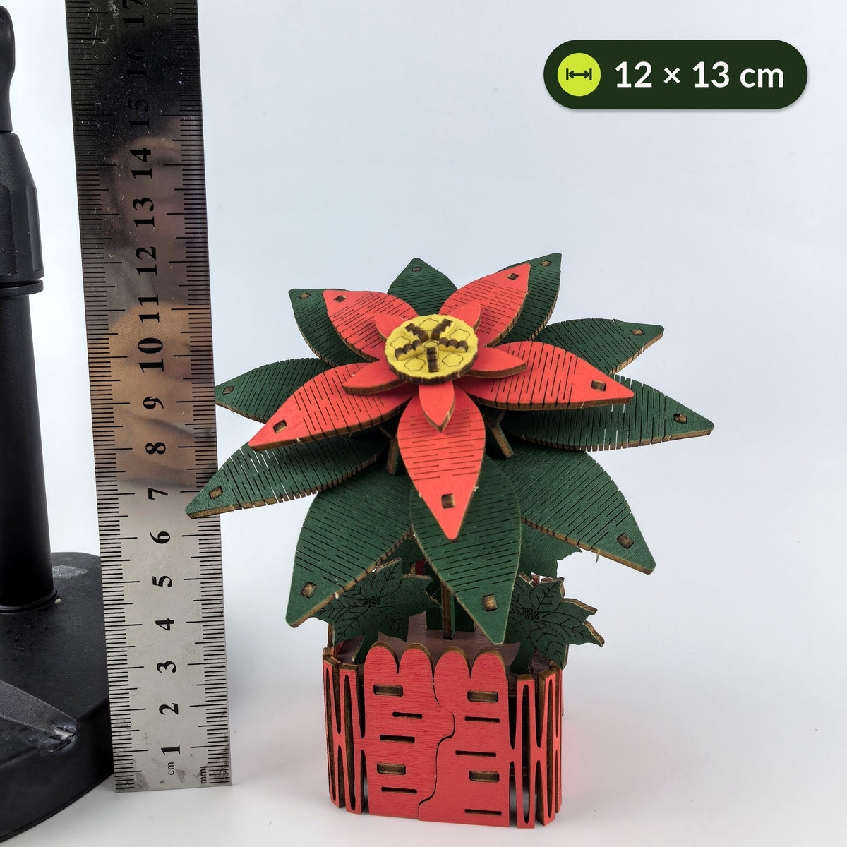 Kleine houten kerstster naast een liniaal, ongeveer 12 cm breed en 13 cm hoog, met een gouden bloemhart