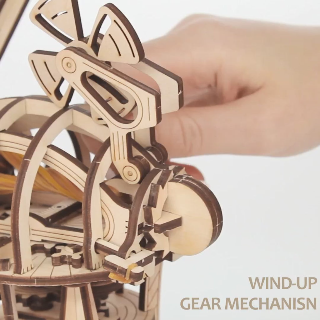 Vidéo : on voit des mains installer la tête d'aile du moulin à vent mécanique en bois, avec des gros plans sur les roues dentées
