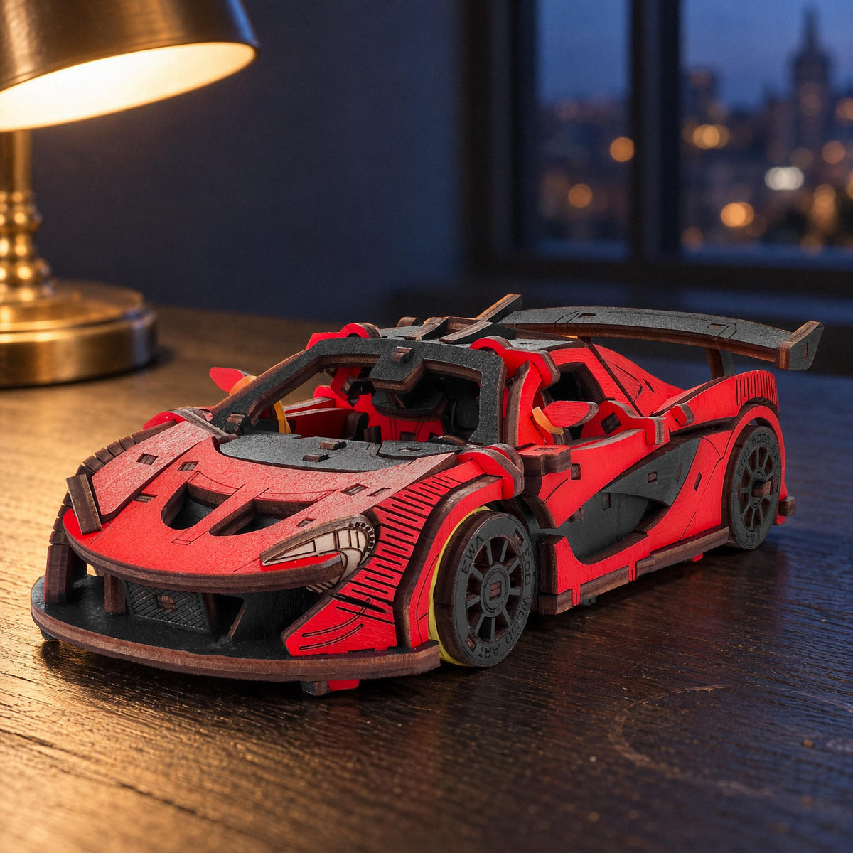 Racing Car, a red wooden model in the evening light on a dark desk with a brass lamp and a view of the city