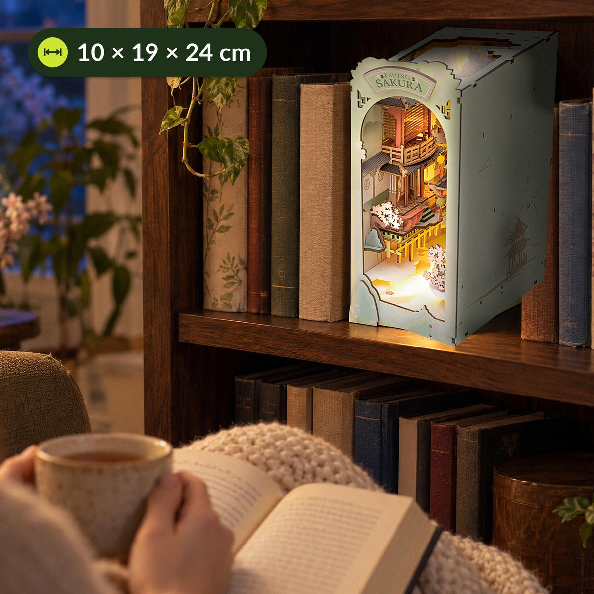 Falling Sakura Book Nook, leuchtet im Wohnzimmerregal, davor Tee und Buch im Sessel, 10 × 19 × 24 cm