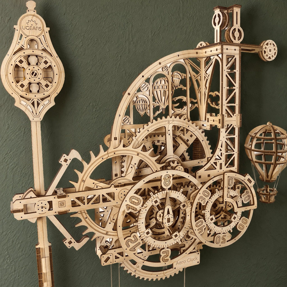 Aero-wandklok met slinger van Ugears, mechanische houten klok, schuin van voren gezien tegen een donkere olijfgroene muur in het daglicht