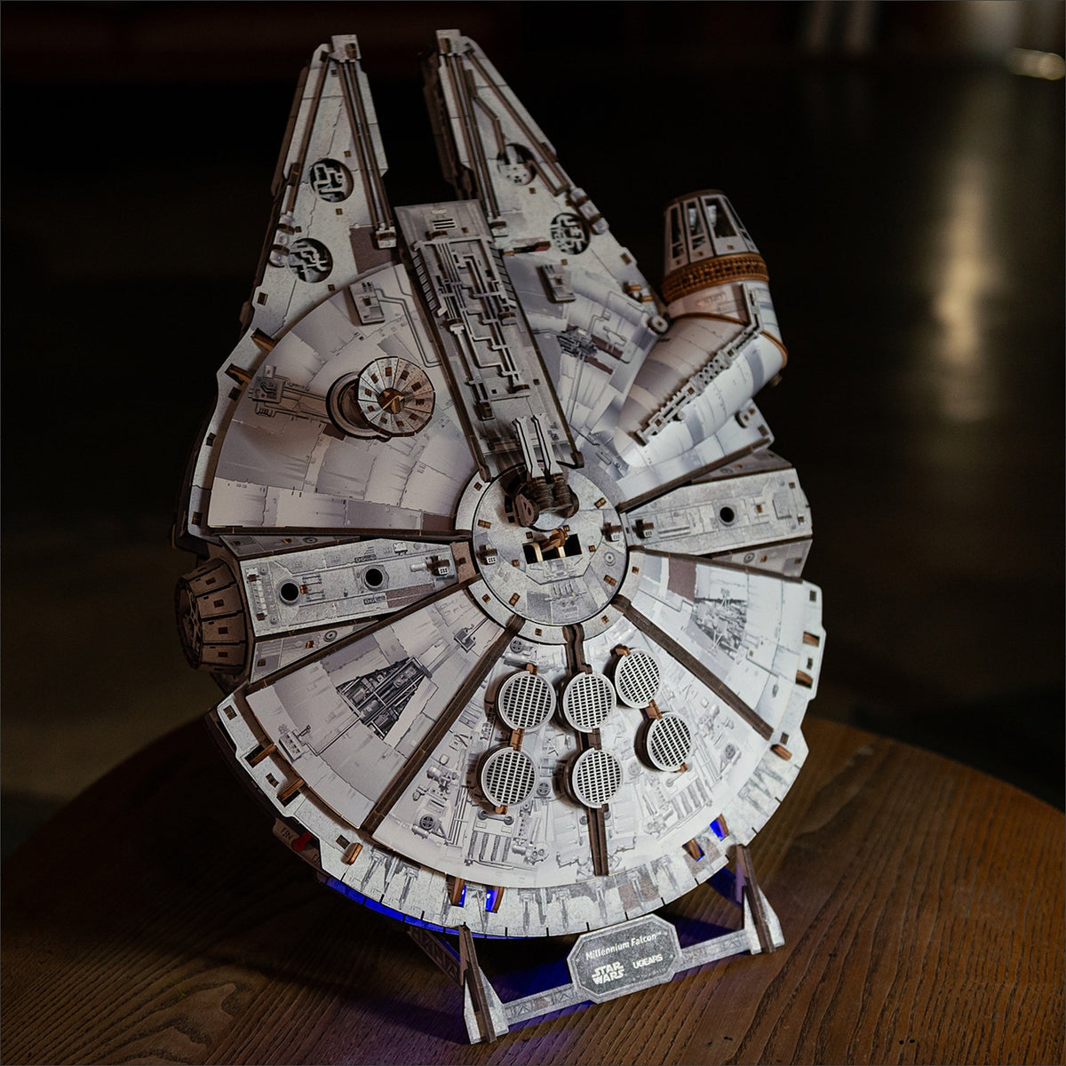 Star Wars Millennium Falcon Maquette en bois, posé bien droit sur son socle, le soir, sur une table en bois sombre