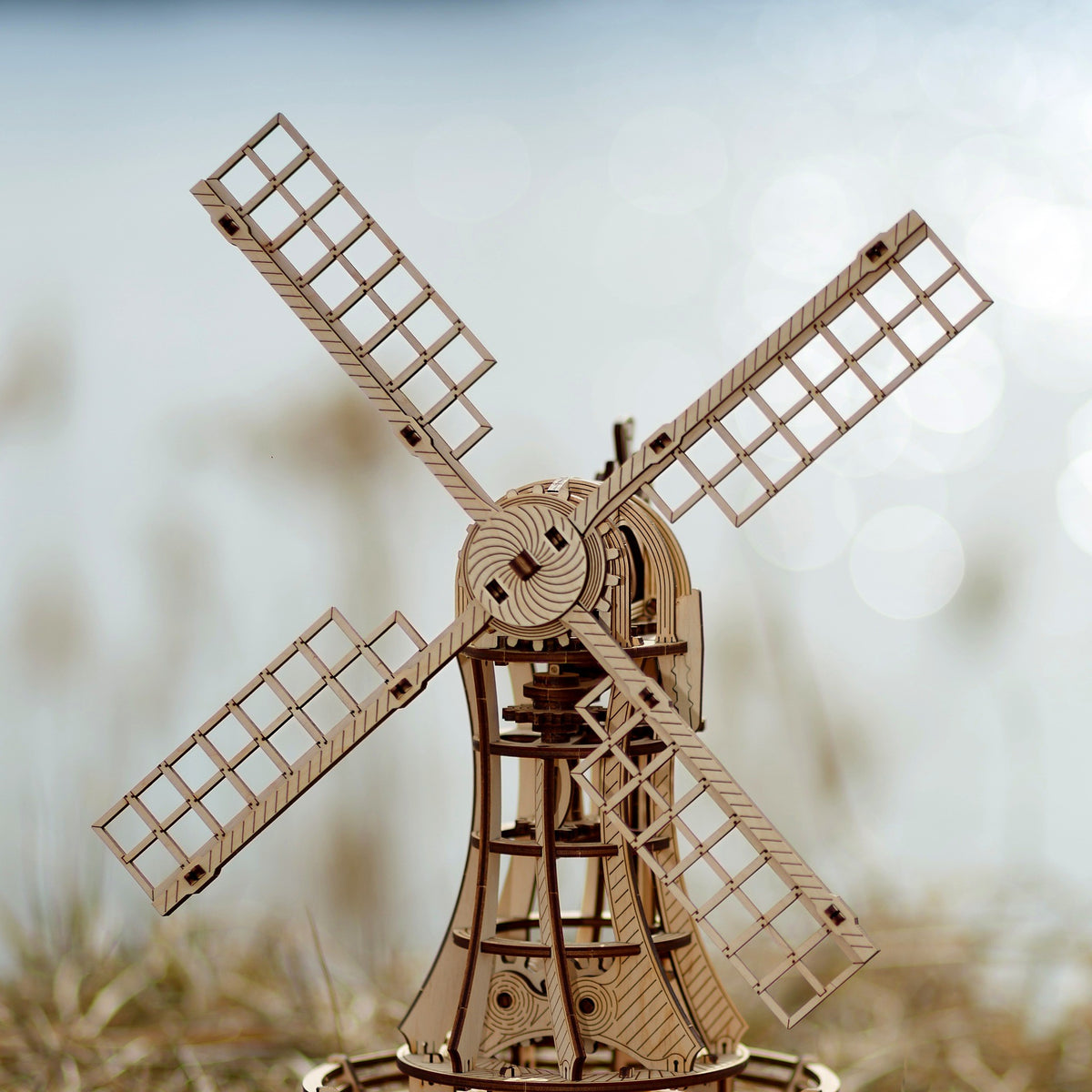 Moulin à vent mécanique en bois, au bord de l'eau, dans la lumière du soir : vraie photo du kit de construction en bois d'Eco-Wood-Art