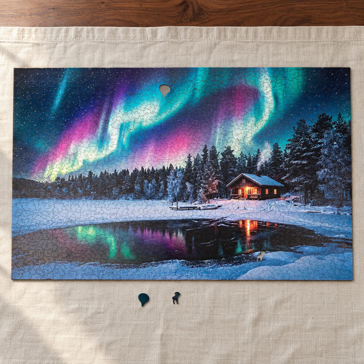 Winterlandschaft XL Holzpuzzle, fast fertig auf einem Leinentuch am Nussbaum-Esstisch, davor die Figurenteile Ballon und Elch